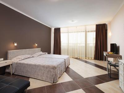 Moderne hotelkamer met twee eenpersoonsbedden, bruine gordijnen, patroonvloer en tv op bureau.