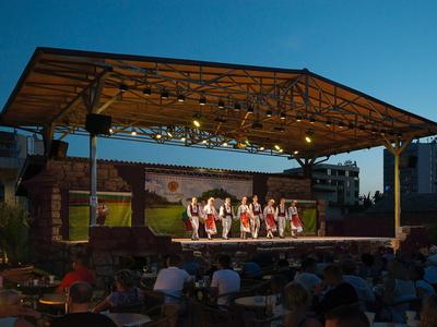 Abendliche Tanzaufführung auf einer überdachten Bühne vor Publikum im Freien.