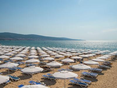 Strand mit vielen weißen Sonnenschirmen und Liegen, blauer Himmel und Meer im Hintergrund.