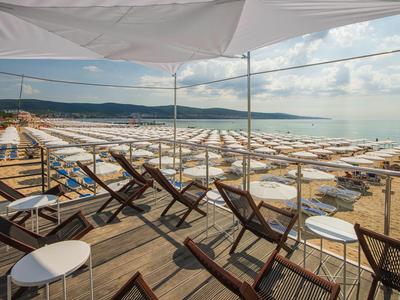 Strand mit vielen weißen Sonnenschirmen und Holzstühlen unter einem Sonnensegel am Strand