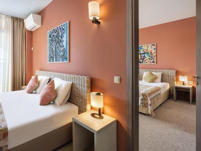 Twee aangrenzende slaapkamers met perzikkleurige muren, beige meubels, wandkunst en nachtlampjes.