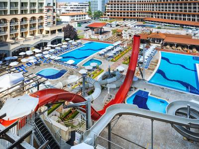 Mehrere Swimmingpools mit Wasserrutschen umgeben von Liegestühlen und Hotelgebäuden.