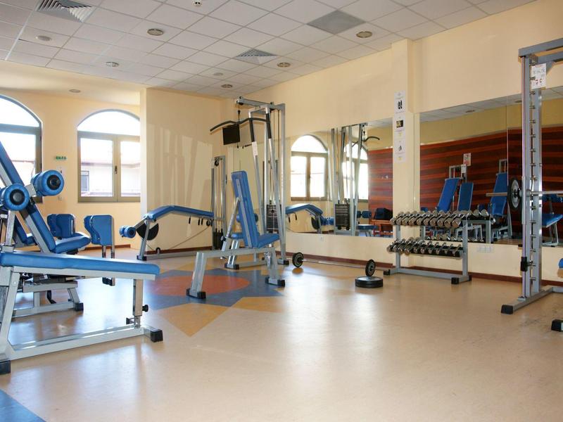 Ruime hotelgym met diverse fitnessapparaten en grote spiegels aan de muur.