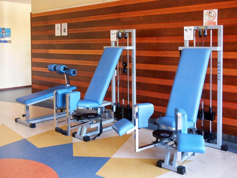 Blauwe fitnessapparatuur in een hotel fitnessruimte met houten wandpanelen en een patroon vloer.