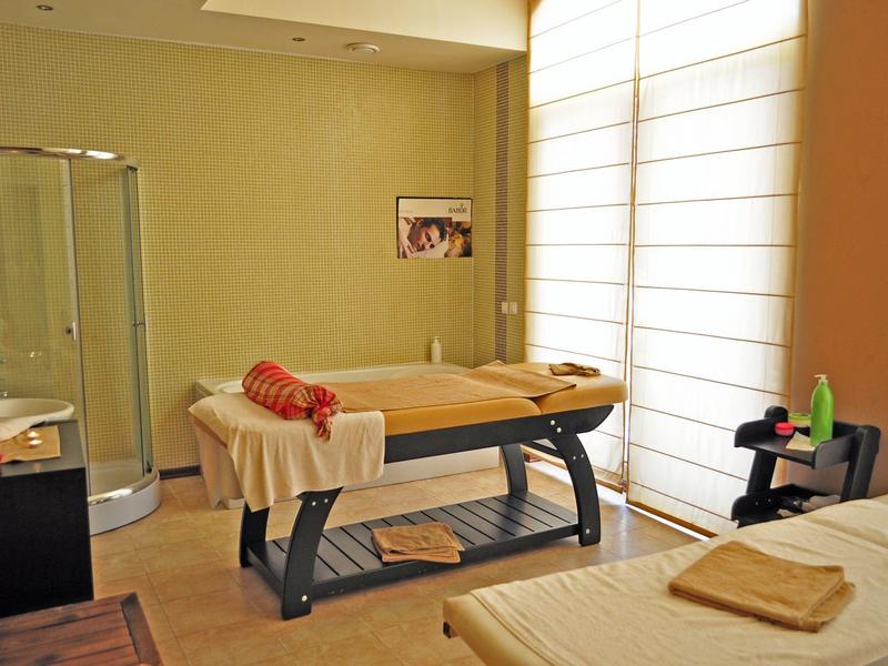 Gezellige massageruimte met twee tafels, zacht licht en een groot raam met jaloezieën.