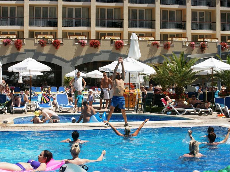 Mensen die bij het zwembad van een hotel met parasols en balkons ontspannen en zonnen.
