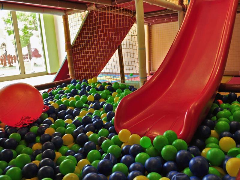 Overdekte speelruimte met een rode glijbaan en een ballenbak vol kleurrijke ballen.