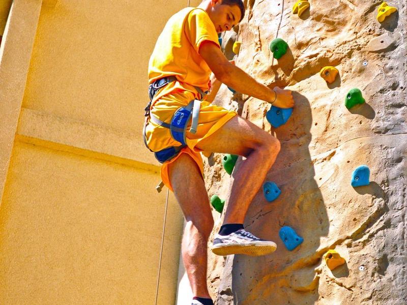 Persoon klimt op een kleurrijke indoor klimwand met een veiligheidsharnas aan.