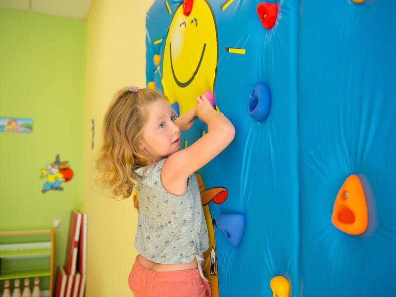 Jong meisje klimt op kleurrijke indoor klimwand met een glimlachend gezicht in een lichte kamer.