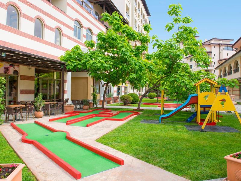 Buiten minigolfbaan en speeltuin voor kinderen in een hotelbinnenplaats met groene bomen.