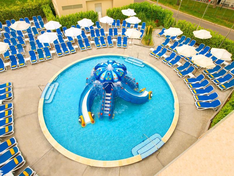 Rond zwembad met blauwe glijbaan en veel blauwe ligstoelen met witte parasols eromheen.