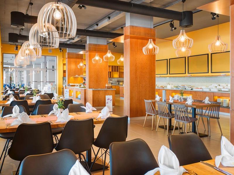 Licht hotelrestaurant met houten tafels, zwarte stoelen en hangende glazen lampen.