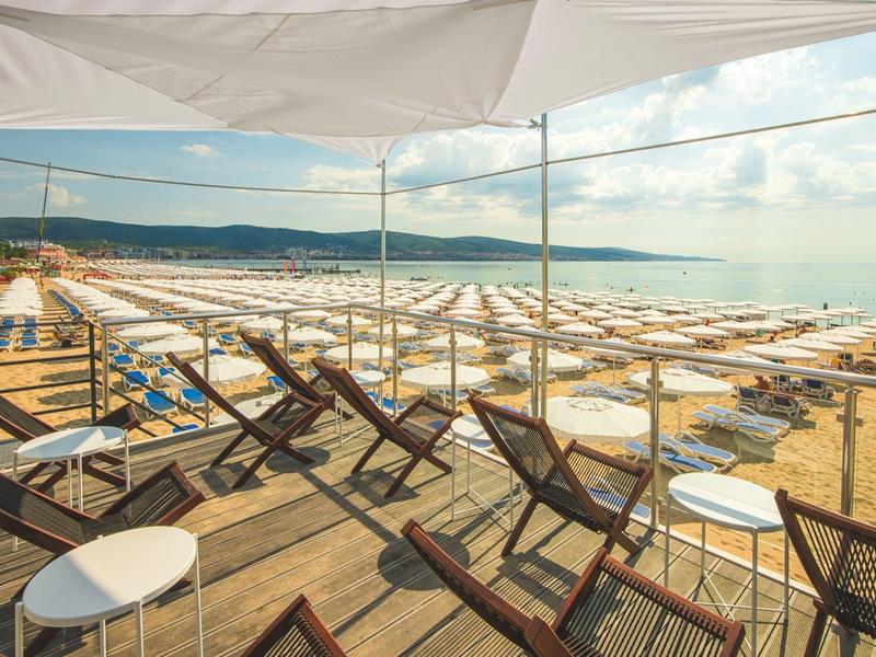 Strandparasolletjes en ligstoelen op een zandstrand aan zee onder een deels bewolkte hemel.