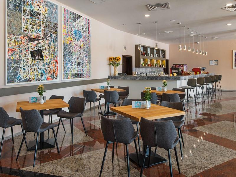 Moderne hotel eetruimte met tafels, stoelen, bar en kleurrijke wandkunst.