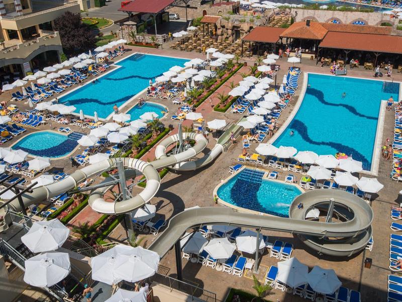 Een groot hotelzwembad met meerdere zwembaden, glijbanen en veel ligstoelen met parasols.