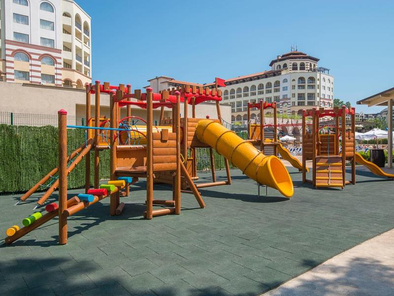 Buitenspeeltuin met glijbanen en klimtoestellen bij hotelgebouwen onder een heldere lucht.