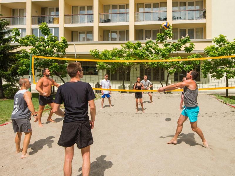 Mensen spelen volleybal op een zandveld voor een hotelgebouw.