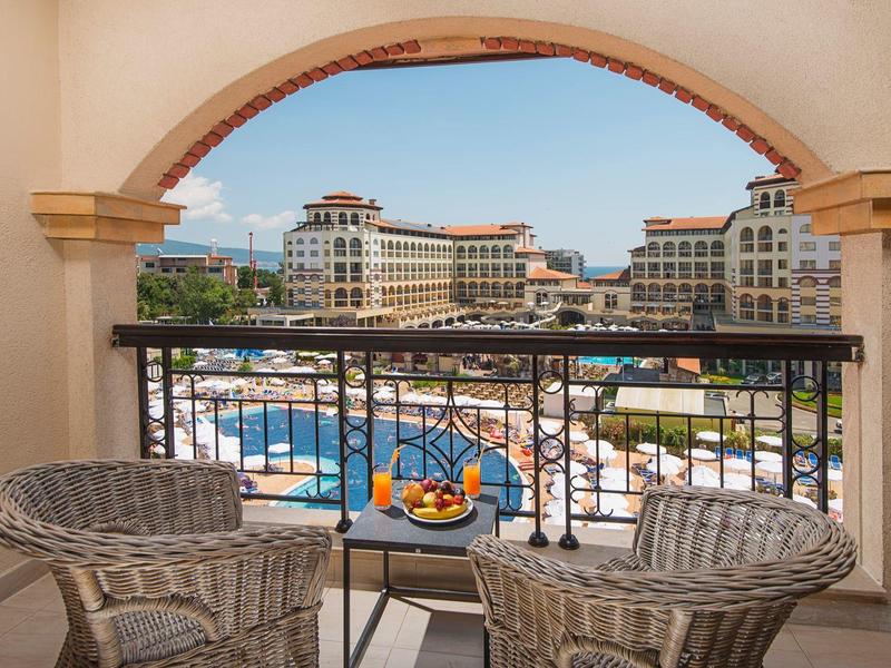 Uitzicht op een hotelzwembad en gebouwen vanaf een balkon met een tafel en twee stoelen.