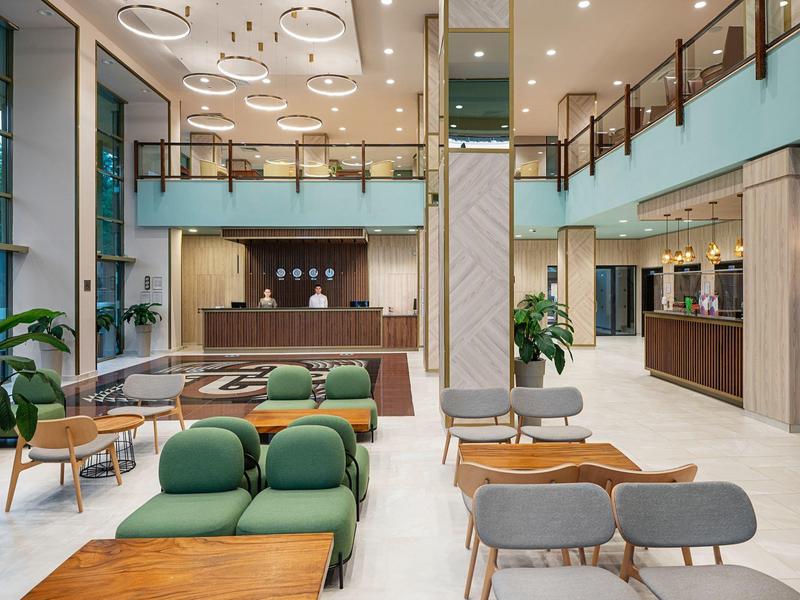Ruime hotel lobby met moderne zitplaatsen, houten tafels en een receptiebalie onder helder licht.