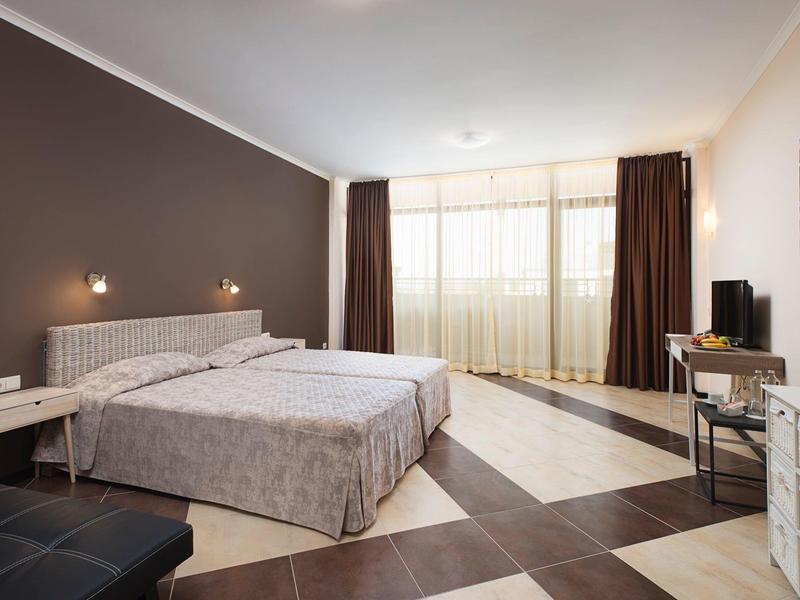 Moderne hotelkamer met twee eenpersoonsbedden, bruine gordijnen, patroonvloer en tv op bureau.