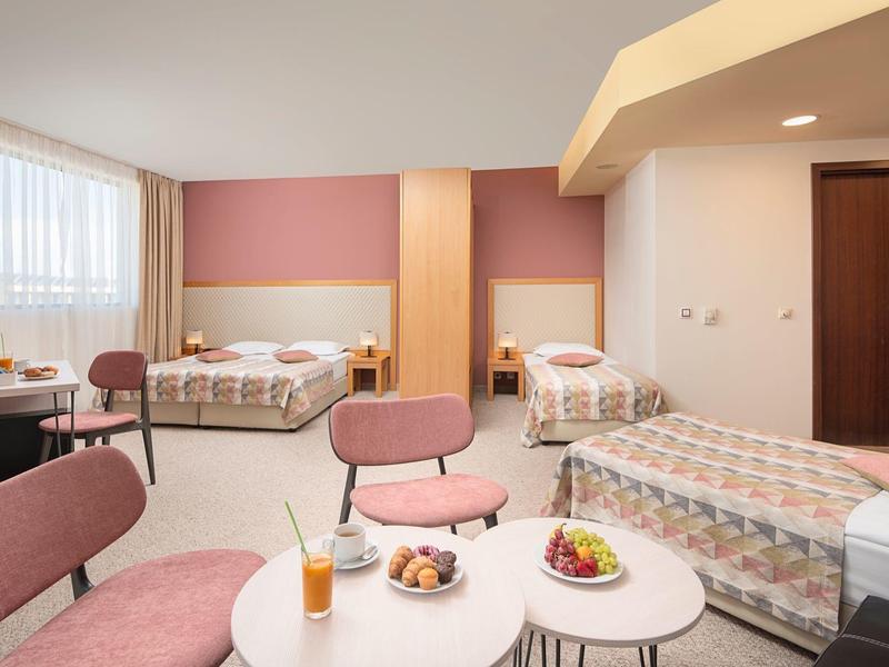 Hotelkamer met twee eenpersoonsbedden, lichtroze muren, gezellige zitplaatsen en een kleine tafel met drankjes en snacks.