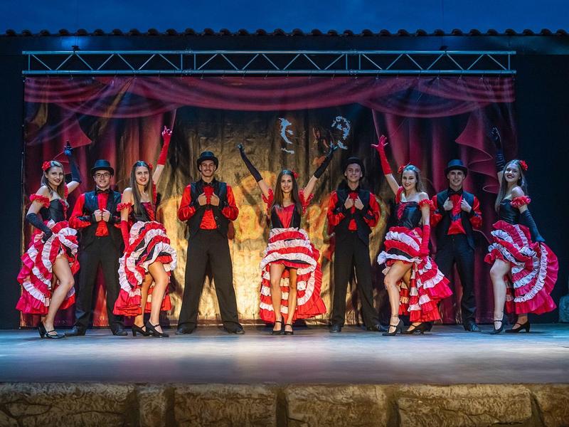 Groep dansers die op het podium optreden in kleurrijke kostuums met rood-witte rokken.