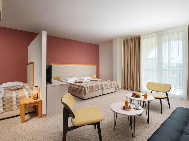 Hotelkamer met twee bedden, een bank, stoelen en een tafel met ontbijt bij grote ramen.