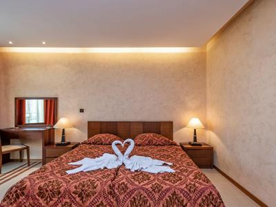 Hotelzimmer mit Doppelbett, dekoriert mit Handtuchschwänen, Schreibtisch und zwei Nachttischen mit Lampen.