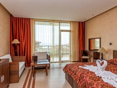 Helles Hotelzimmer mit Doppelbett, Balkon und Schreibtisch, dekorativem Bettbezug und Tageslicht.