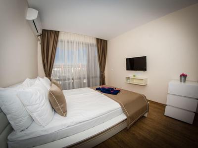Modern hotel room with double bed, TV, and large windows with brown curtains.
