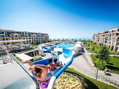Multi-story hotel resort with large pools and water slide under blue sky