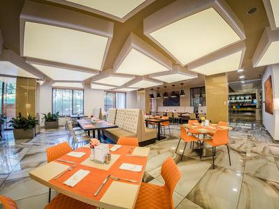 Helles Hotelrestaurant mit orangefarbenen Stühlen und modernen Marmorböden.