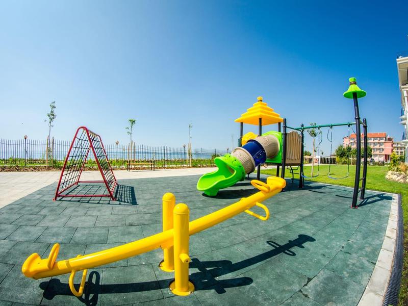 Colorful modern playground with slide and seesaw next to a hotel building in sunshine.
