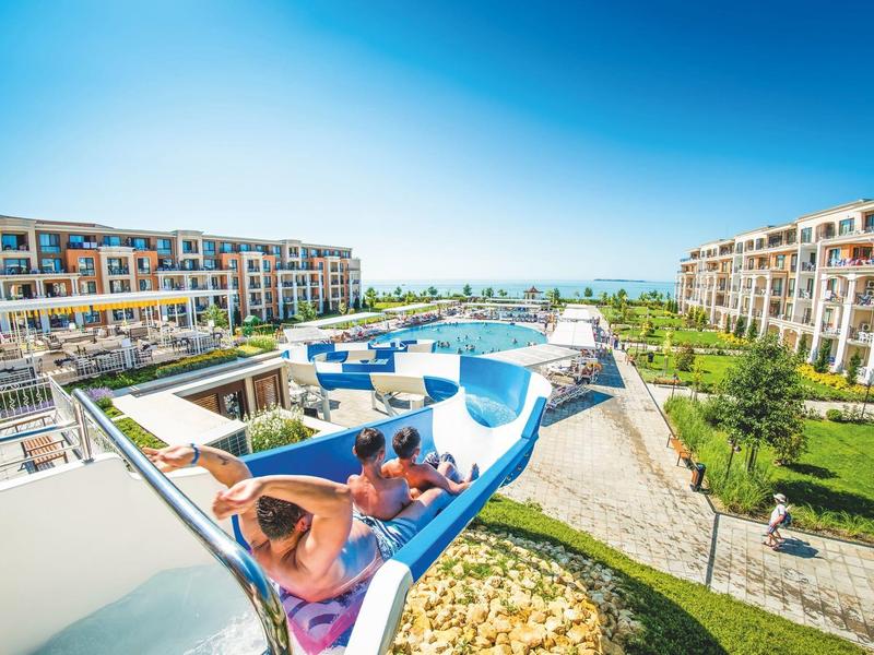 Several people sliding down a water slide at a resort on a sunny day.