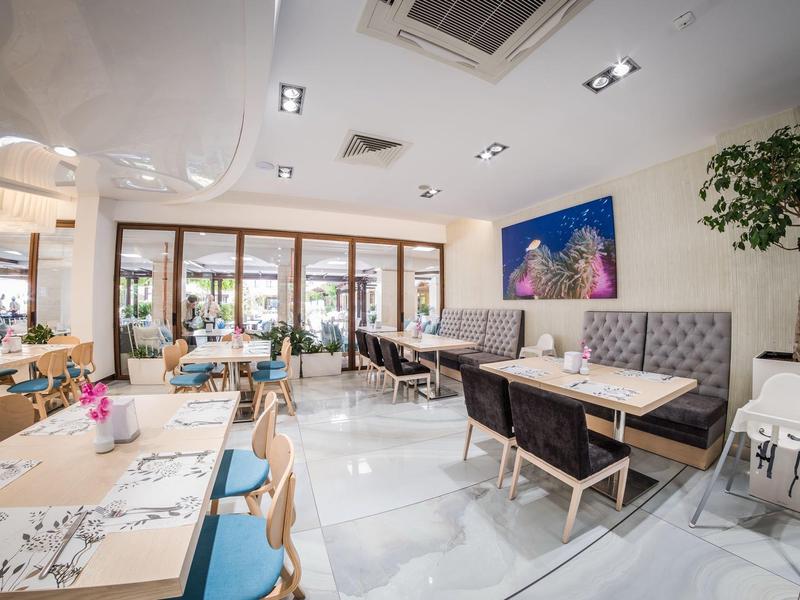 Bright, modern restaurant lounge with large windows, various seating areas, and decorative plants.