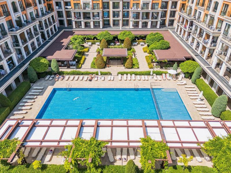 View of a hotel pool with sun loungers and manicured garden in an inner courtyard.