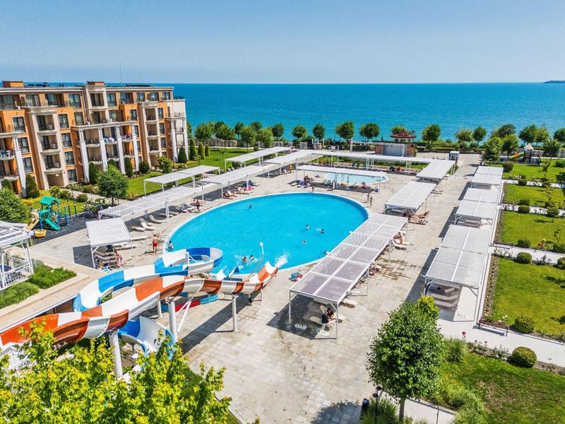 Modern hotel complex with large outdoor pool, water slides, and sea view.