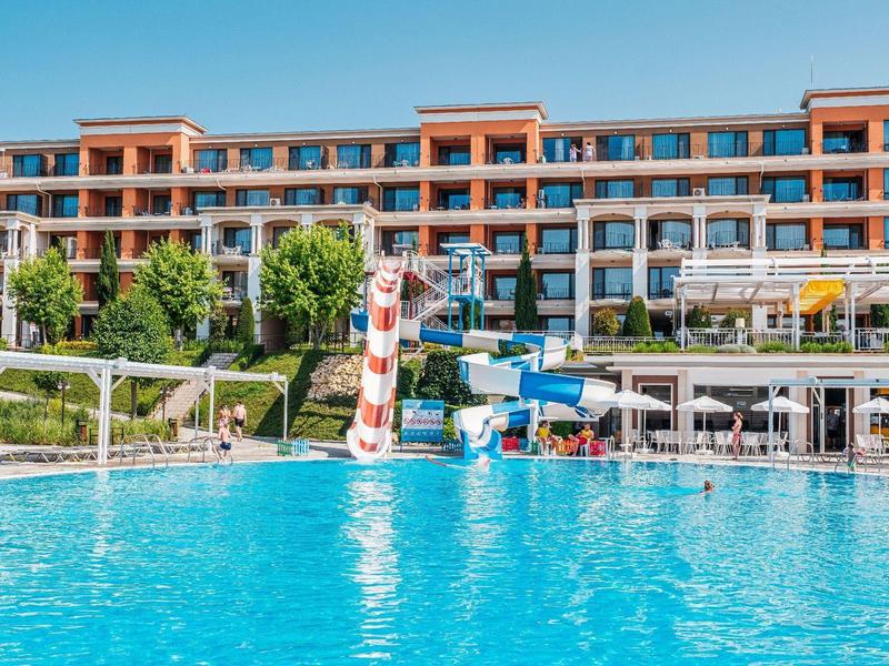 Large hotel with pool, water slides, and loungers on a sunny day.