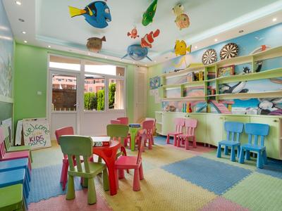 Buntes Kinderspielzimmer mit kleinen Tischen, Stühlen, Teppich und Tier-Dekoration an der Decke.
