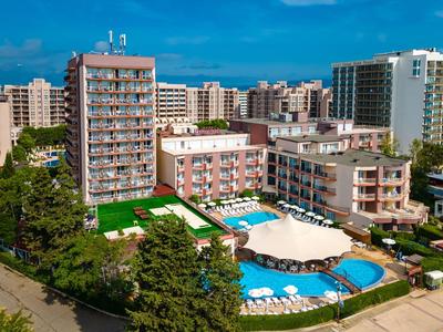 Große Hotelanlage mit mehreren Gebäuden, grünem Garten und zwei blauen Schwimmbecken bei klarem Himmel.