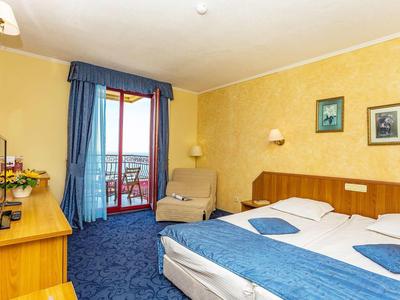 Bright hotel room with double bed, blue carpet, and balcony overlooking the sea.