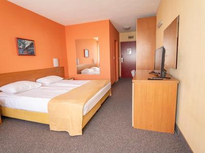 Modern hotel room with double bed, orange walls, and flat-screen TV on wooden dresser.