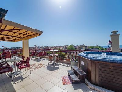 Dachterrasse mit Whirlpool, Sitzbereich, mehreren Tischen und Stühlen unter blauen Himmel.