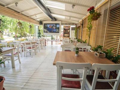 Helle offene Terrasse eines Cafés mit Holztischen, Stühlen und Pflanzen