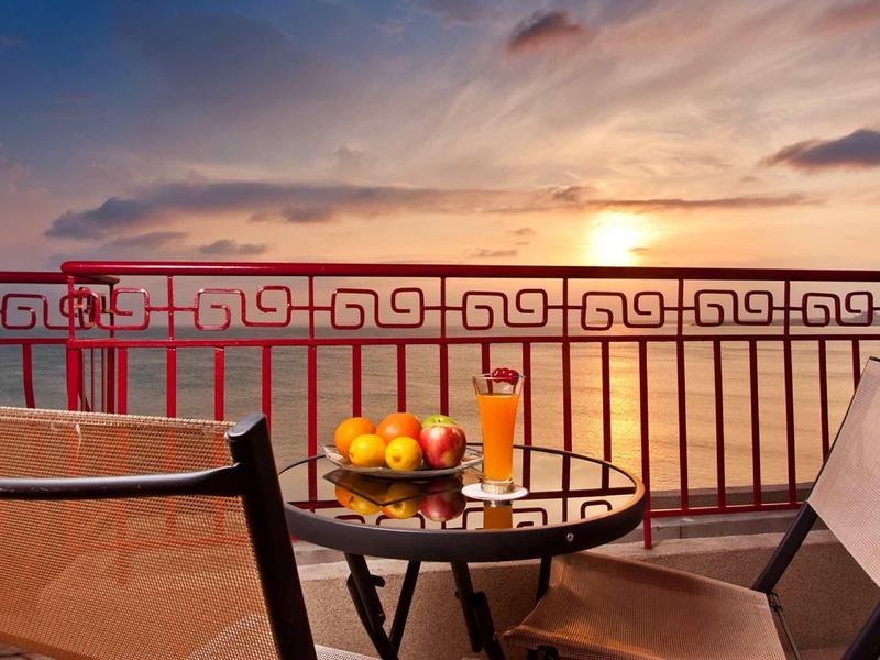Balcony with table and chairs, fruit bowl and drink, sea view at sunset.