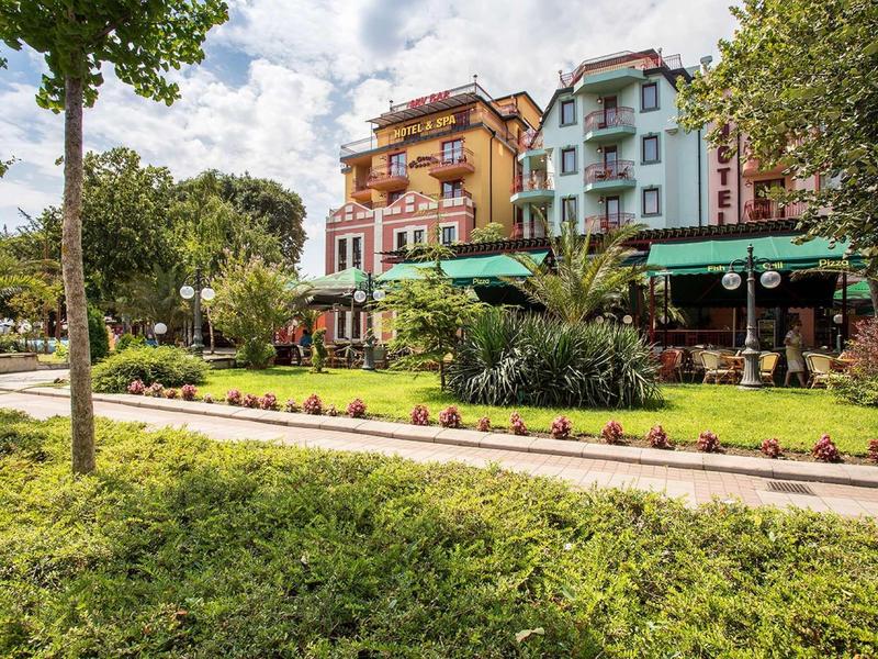 Colorful hotel buildings with outdoor dining and well-kept garden under cloudy sky.