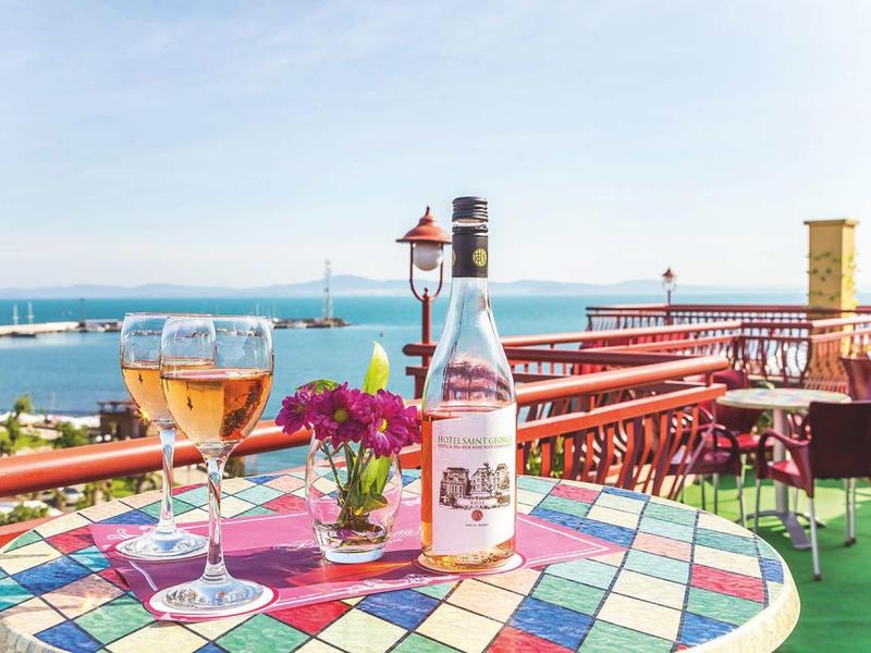 Table with wine glass, water bottle, and flowers on terrace overlooking the sea