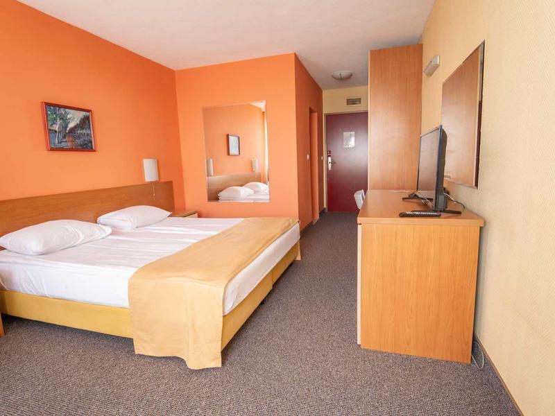 Modern hotel room with double bed, orange walls, and flat-screen TV on wooden dresser.