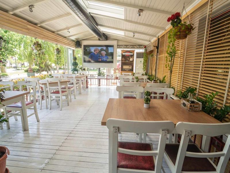 Bright, open terrace with covered tables and chairs surrounded by plants in a hotel.