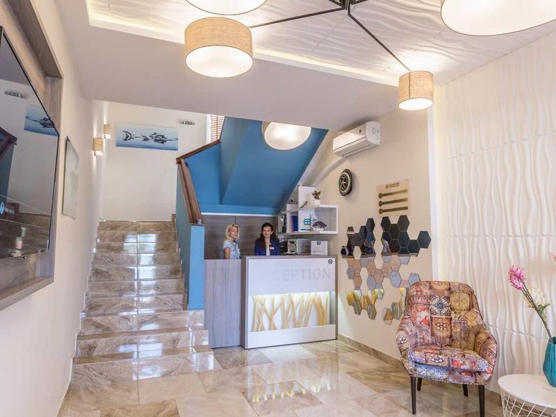 Lichte hotellobby met glanzende marmeren vloer, receptiebalie en moderne plafondlampen.